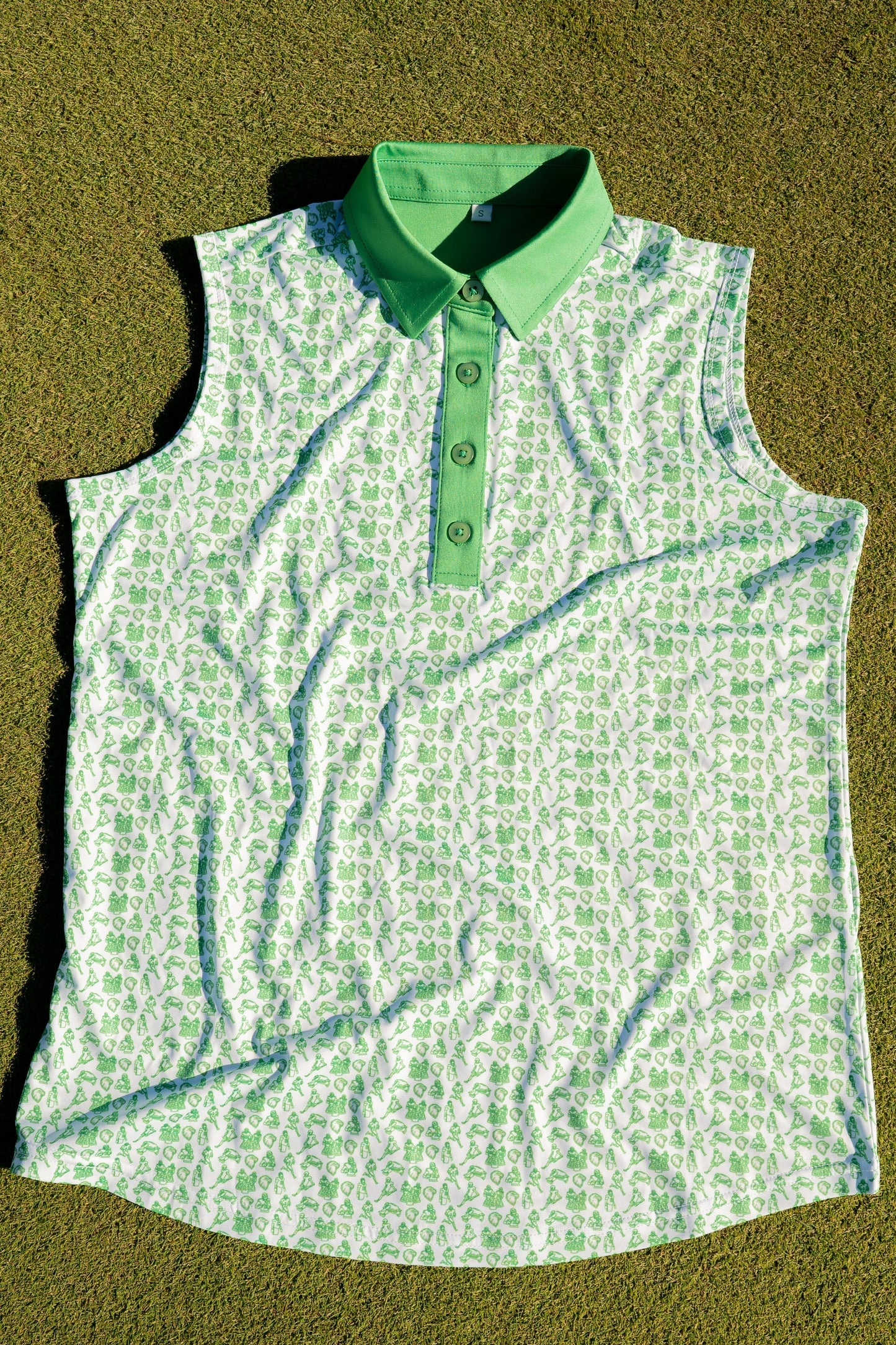 Birds & Beauties women’s golf polo by Foresome Golf Co. laying flat on a putting green near a golf hole